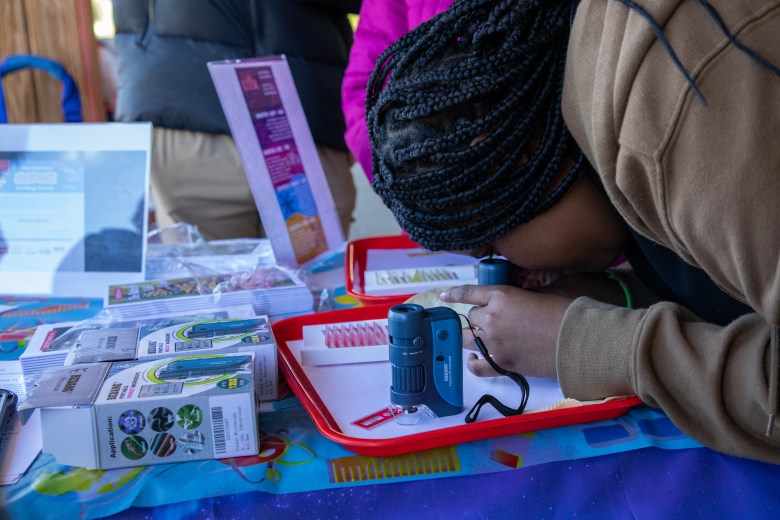 Student uses a pocket microscope to see small organisms at the #SteamtheBlock Party.
