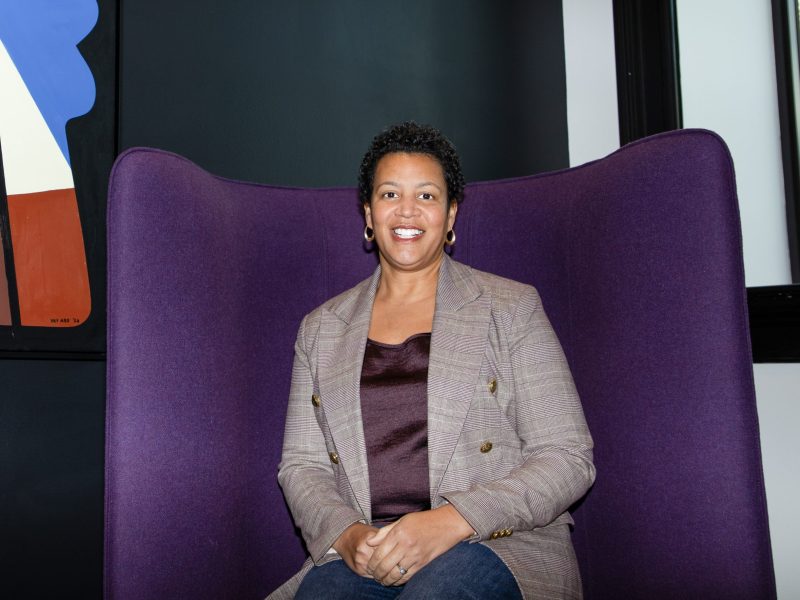 Kristy Love seated in a purple high-back chair, smiling during a portrait session.