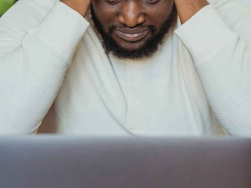 sad black man with hands on head near laptop