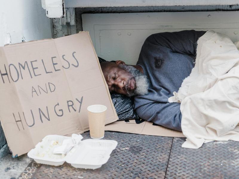 photo of a homeless man sleeping near a cardboard sign